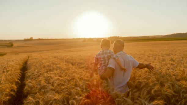 istock Father Carrying Son Through Golden Wheat Field at Sunset 2203778202