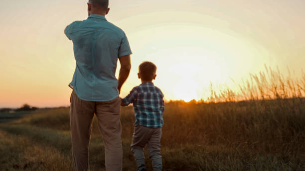 istock Caucasian Father and Son Walking in Wheat Field at Sunset 2203778208