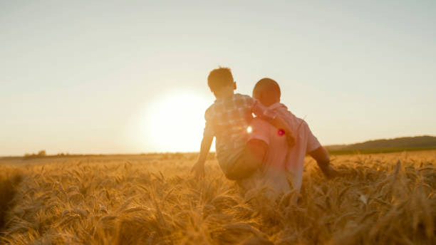 istock Father and Son Walking Through Golden Wheat Field at Sunset 2203778220