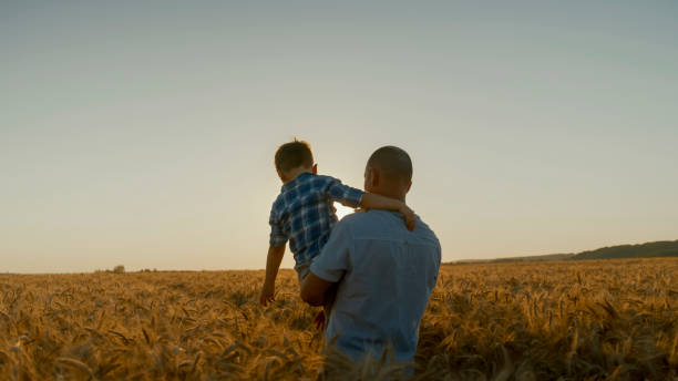 istock Father Carrying Son Through Golden Wheat Field at Sunset 2203778224