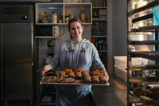 istock Smiling baker proudly displaying a tray of assorted pastries in a commercial kitchen, showcasing her passion for baking 2203779917