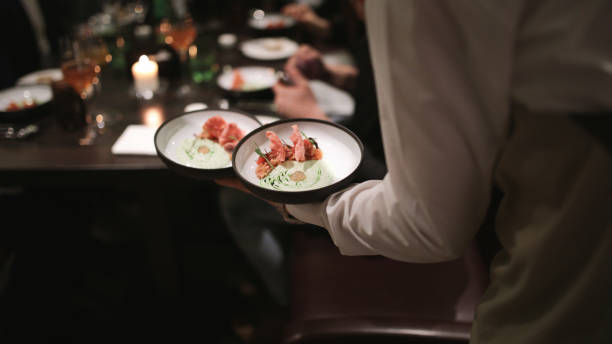 Waiter bringing out two bowls of a crudo to a crowded table Waiter bringing out two bowls of a crudo dish on one hand during busy seafood night at the restaurant. busy restaurant tables stock pictures, royalty-free photos & images