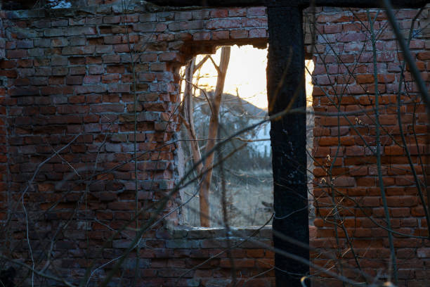 The window has an irregular shape, and the glass is completely missing. Through the opening in the window, a landscape with trees and possibly mountains in the background is visible.