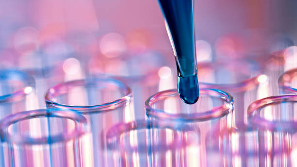 A laboratory pipette carefully releases a blue liquid into multiple transparent test tubes. The image represents biochemical research, pharmaceutical testing, and scientific analysis in a modern laboratory setting.