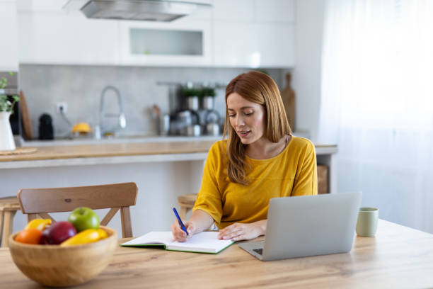 istock Focused Woman Writing in Home Workspace with Laptop and Notes 2203783887