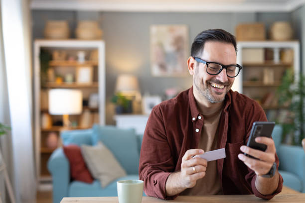 istock Happy man smiles while holding a card and looking at phone. 2203784987