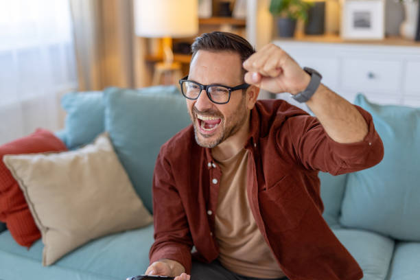 istock Cheerful man on couch celebrates a happy moment with TV 2203785036