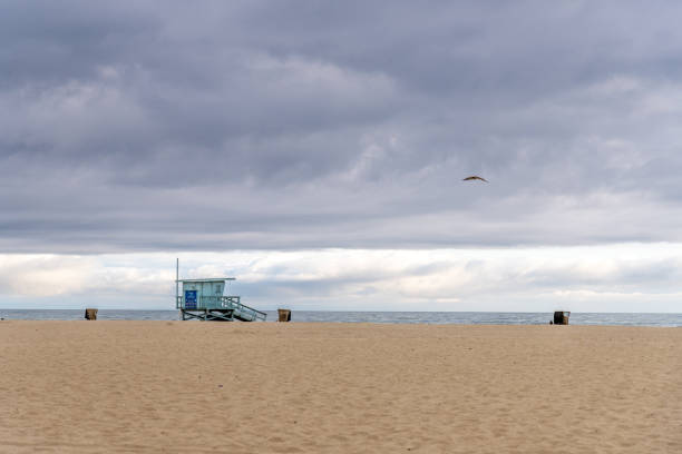A beautifully serene beach landscape featuring a lifeguard tower set against a moody, dramatic sky above in Santa Monica Beach, California