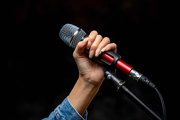 istock Woman hand holding red dynamic microphone on stand isolated on black background. 2203795021
