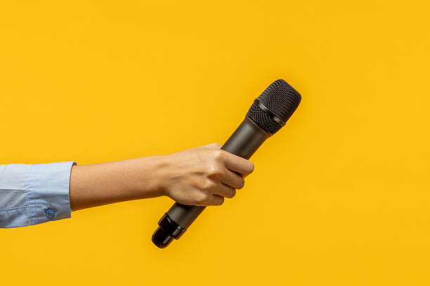 istock Woman hand holding a wireless microphone isolated on yellow background. 2203795041