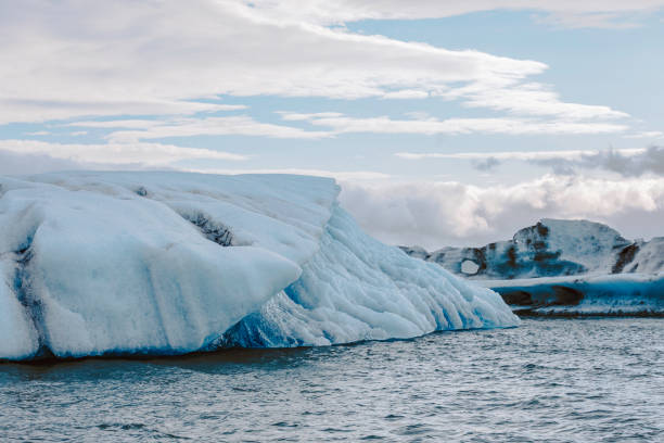 A striking view of a massive iceberg floating in the cold waters of Jokulsarlon Glacier Lagoon in Iceland. The icy formations, sculpted by nature, display intricate textures and shades of blue and white. This breathtaking glacial landscape is part of the Vatnajökull National Park, where melting ice from the Breiðamerkurjökull glacier drifts into the lagoon before heading to the Atlantic Ocean. A must-visit destination for nature lovers and photographers capturing Iceland’s raw beauty