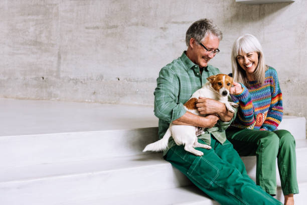 A joyful couple in their 60s sits together on modern white steps, sharing a warm moment with their adorable dog.
