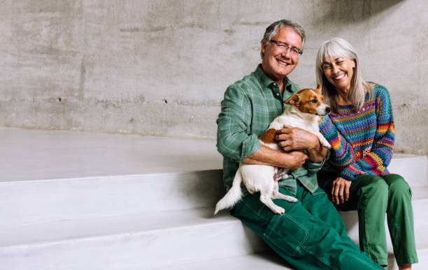 istock A joyful couple in their 60s sits together on modern white steps, sharing a warm moment with their adorable dog. 2203798703
