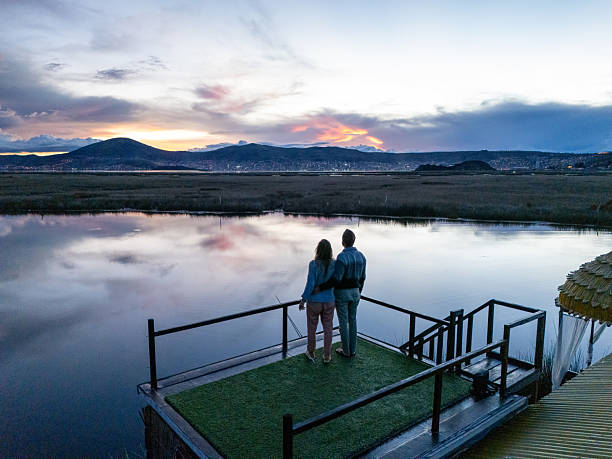 Romantic couple standing on a dock overlooking a serene lake at sunset. Peaceful evening view with mountains in the distance. Scenic getaway for nature lovers.