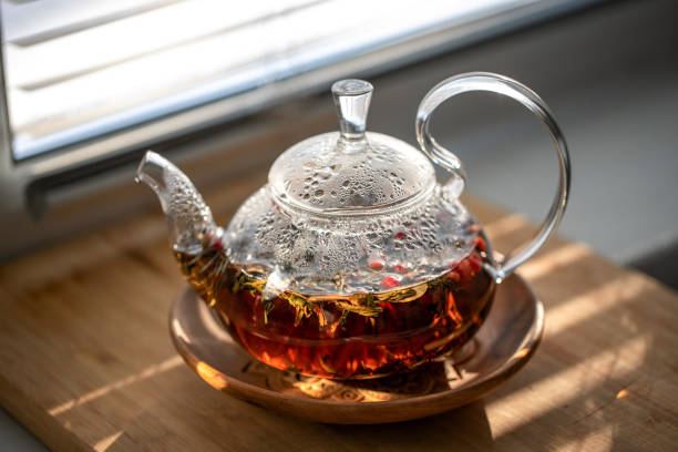 istock Glass teapot with fragrant berry tea, standing on the windowsill. Front view 2203802201