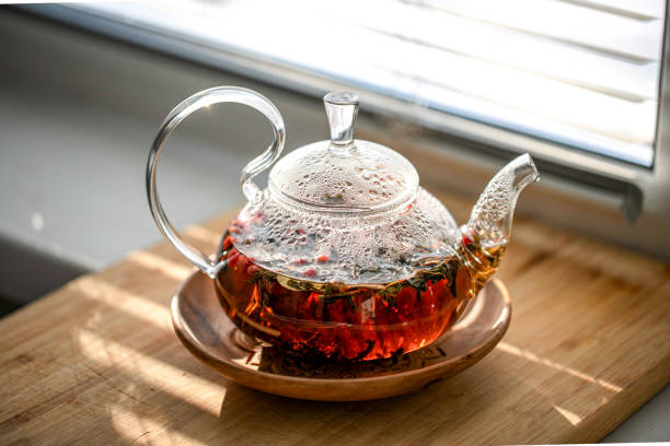 istock Glass teapot with fragrant berry tea, standing on the windowsill. Front view 2203802375