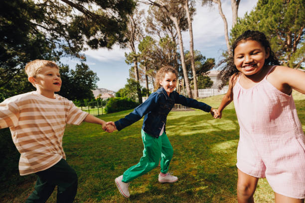 istock Children holding hands and playing together outdoors in a park 2203804223