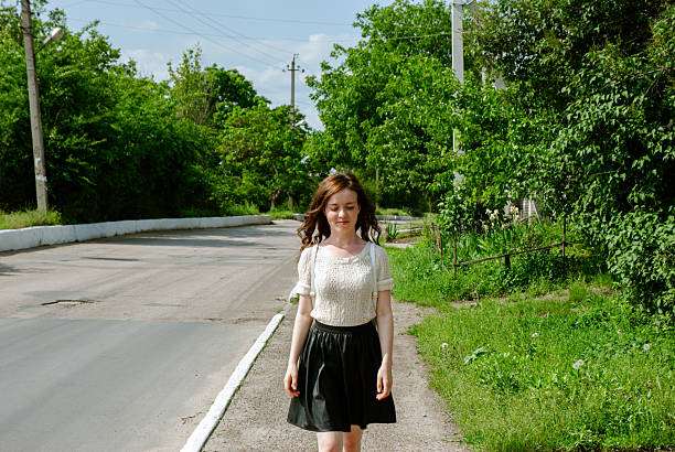 Young caucasian female walking on a tree-lined road on a sunny day.