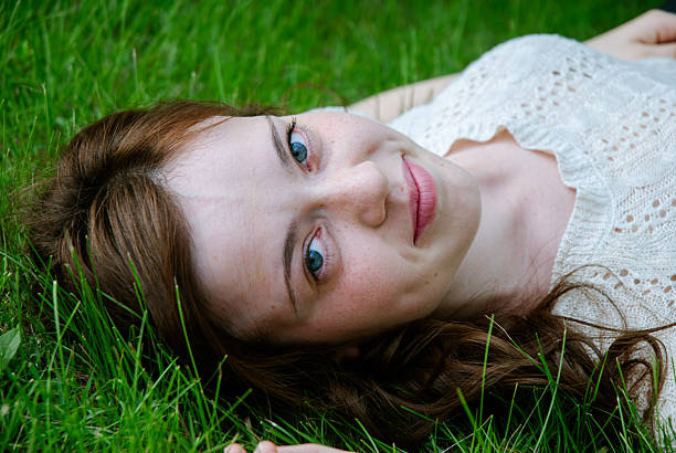 close-up portrait of a pretty blonde girl with long hair and light eyes lying on the lawn of a garden looking at the camera smiling