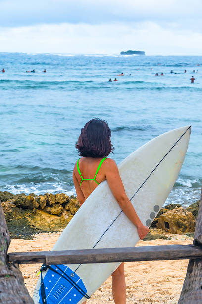Female surfer holding her surfboard and watching the waves at the beach in siargao island, philippines