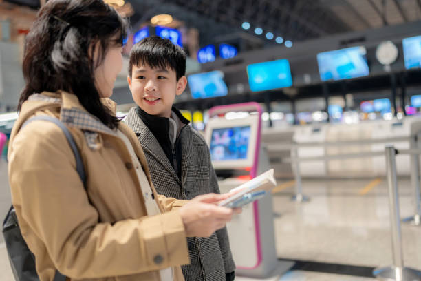 A mother and her young son check in for their flight using a self-service kiosk at the airport. They review their passports and boarding details, embracing technology for a seamless travel experience. Perfect for themes of travel, efficiency, and bonding.