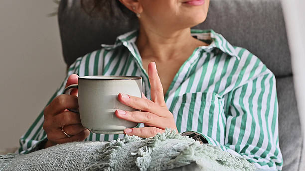 A woman enjoys a warm coffee while working remotely from her comfortable and cozy home office, embracing a relaxed and productive lifestyle. Her striped shirt complements the serene ambiance.