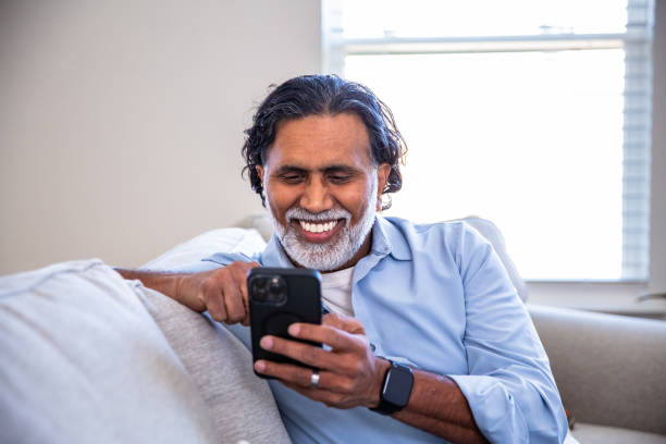 istock Mature Indian man at home smiling using his smartphone on couch 2203824205