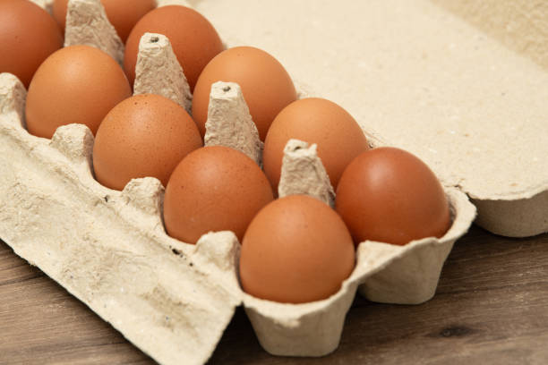 istock A dozen brown eggs rest in a cardboard carton, showcasing their smooth shells. The eggs are arranged evenly on a light wooden table, emphasizing freshness and quality 2203824909