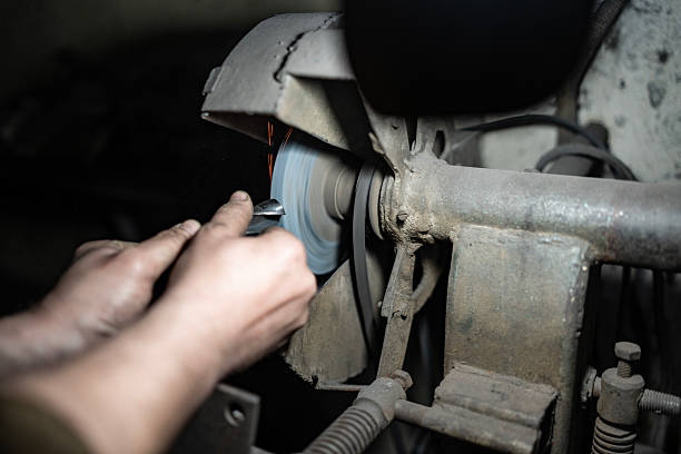A detailed view of a craftsman using a grinding wheel to sharpen a metallic object, showcasing the technical precision involved in workplace craftsmanship and the industrial context of metalworking.