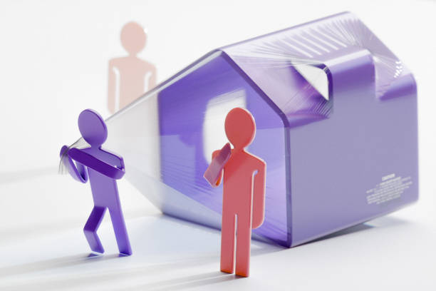 A purple figure struggles to pull a plastic-wrapped house while another person observes, representing the challenges of mortgage debt and the strain of home ownership costs.
