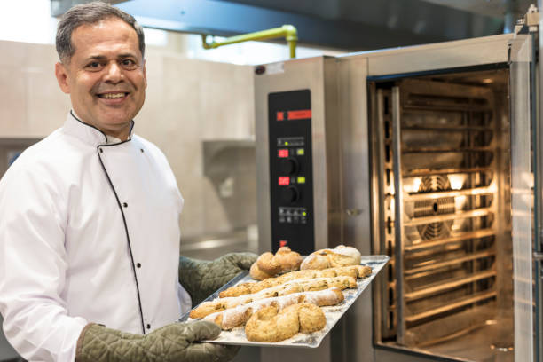 istock Male  baker in uniform taking fresh breads out from oven 2203837834