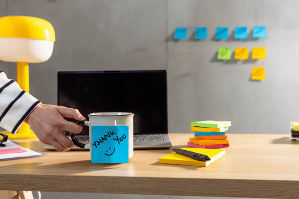 A well-organized desk setup with a focus on a mug with a handwritten 'thank you' note and colorful sticky notes, creating an ambience of gratitude and efficiency.