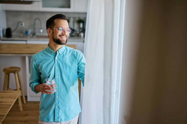 istock Young man drinking water and looking out the window at home 2203840365