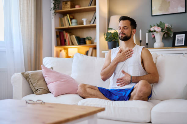 istock Young Man Practicing Breathing Exercises on Sofa at Home 2203840554