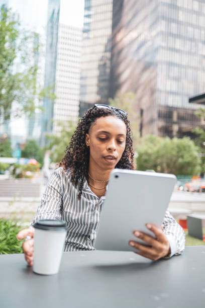 istock Woman in professional attire reading a tablet outdoors with a coffee cup 2203844603