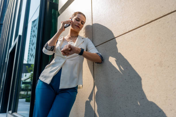istock professional woman checking her watch while talking on smartphone, dressed in stylish outfit, standing against modern building. She exudes confidence and focus 2203866914