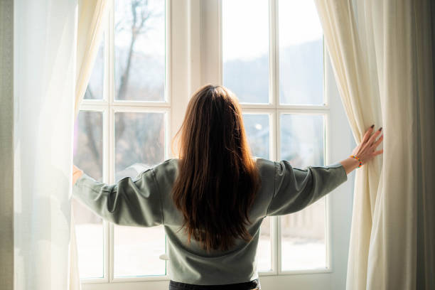 a woman is pulling back the curtains so that the sun can enter the room