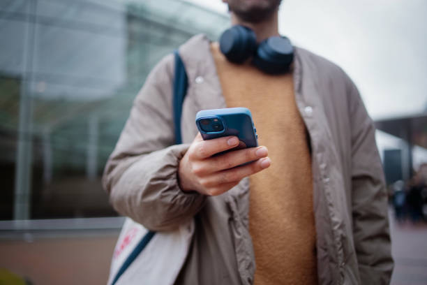 istock Man Using Smartphone Outdoors Wearing Headphones and Carrying a Tote Bag 2203869415