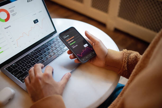 istock Person Using a Smartphone and Laptop to Analyze Financial Graphs in a Workspace 2203869443