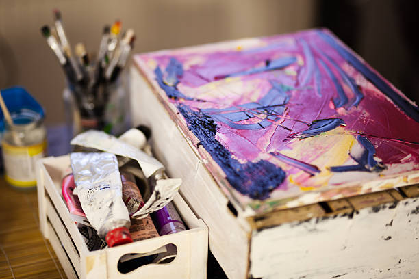 An intimate glimpse into an artist's studio featuring a vibrant abstract painting on canvas alongside a collection of brushes, paint tubes, and art tools.