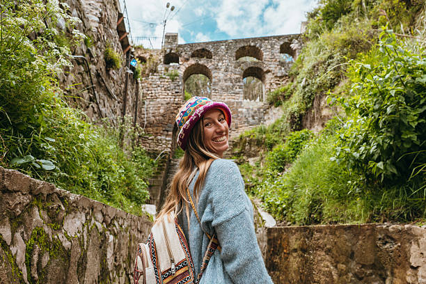 Young woman in vibrant hat smiles while walking through historical stone ruins. Tourist enjoying nature and architecture. Exploring ancient landmarks.