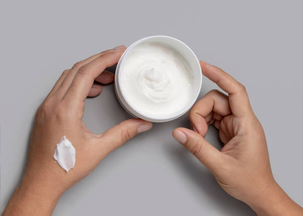 istock Female hands holding opened cream jar over grey background top view, negative space 2203891482