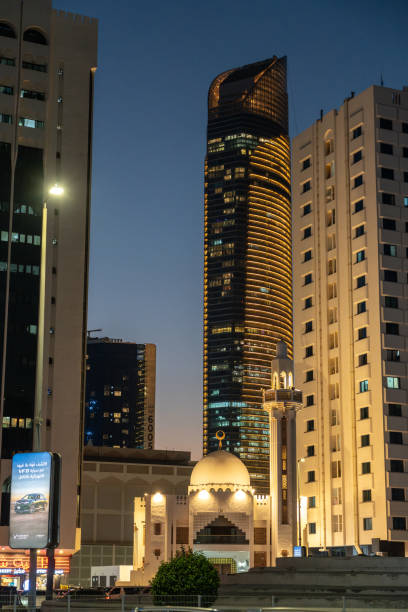 Abu Dhabi, UAE, January 28, 2025: A night view of Abu Dhabi with a modern skyscraper, illuminated mosque, and surrounding buildings, editorial image