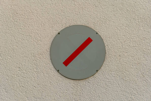 A circular sign with a bold red horizontal stripe is mounted on a light-colored textured wall, signaling no entry for vehicles or pedestrians.