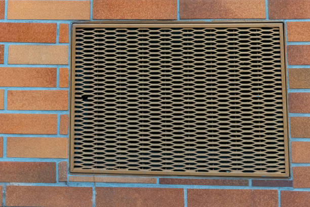A metallic vent cover is installed on a textured brick wall, showcasing a honeycomb pattern. The vibrant bricks provide a striking backdrop in a lively city environment.