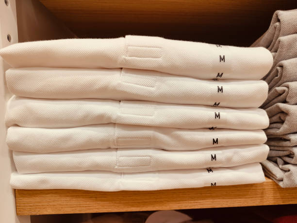 A stack of white shirts with the letters M and M on them. The shirts are piled on top of each other