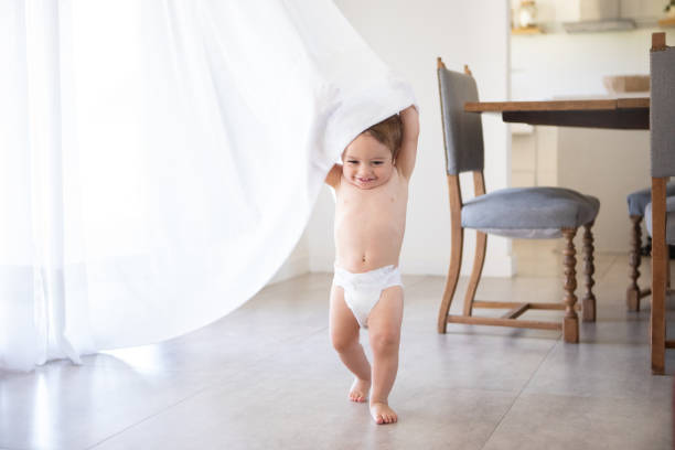 istock Cute baby boy in diapers hiding under the curtains 2203897399