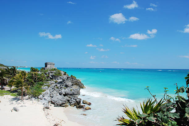 Tulum unites ancient Maya ruins with breathtaking Caribbean coastline. Stone temples perch dramatically on limestone cliffs above pristine white beaches and impossibly turquoise waters. Visitors descend wooden staircases to swim in crystal-clear seas beneath ancient watchtowers, creating a perfect blend of history and natural paradise.