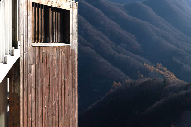 The wall of a wooden house is sheathed with brown horizontal planks. There is a small square window with a casing and an oblique roof shade. Background.