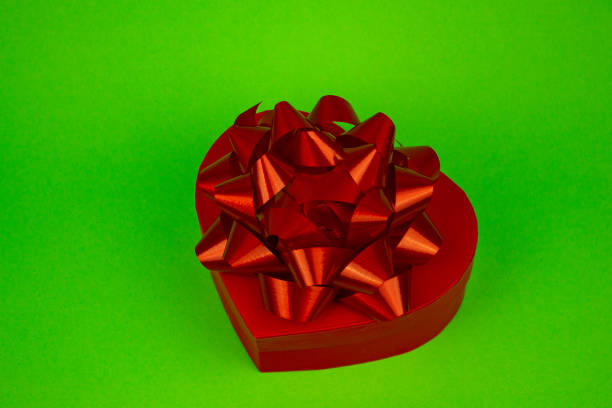 Red heart-shaped box with red bow close-up on green background. High quality photo